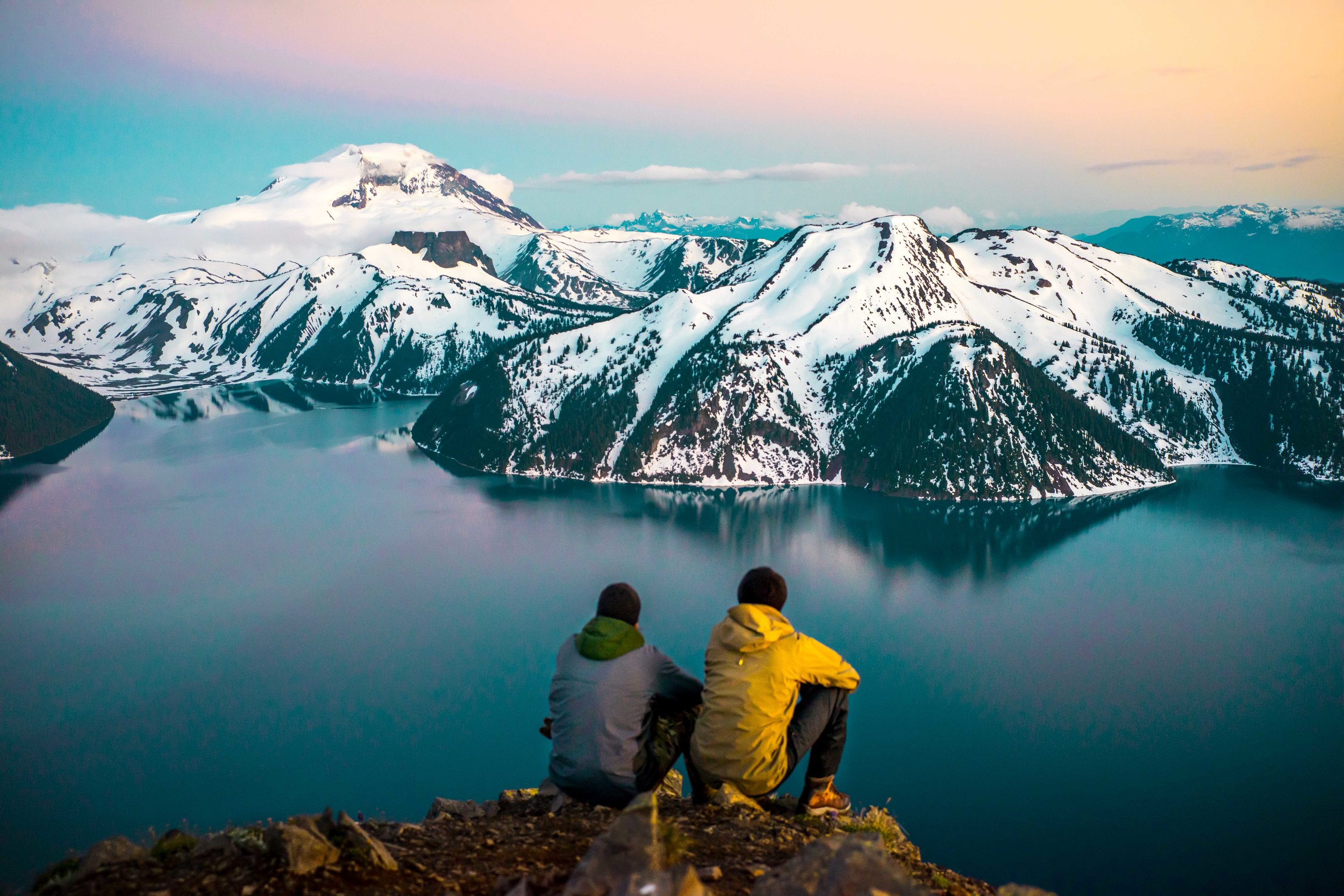 Two figures sitting at the edge of Garibaldi Lake, watching the mountains at dusk